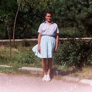 Girl stands on a road with a weeping willow tree.