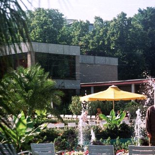 Four people stand in a garden with fountains and chairs.