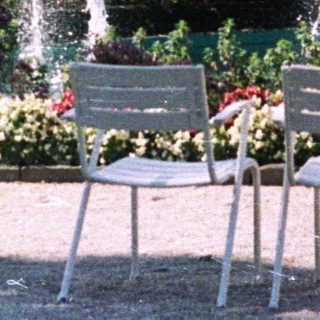 Four people stand in a garden with fountains and chairs.