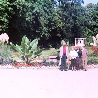 Three people stand in a lush, flower-filled garden.