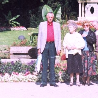 Three people stand in a lush, flower-filled garden.