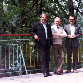 Here's a brief summary of the image: Four men and a woman stand near a railing with a bench.