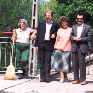 Four people stand on a patio overlooking a river.