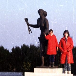 Two people stand near a statue on a snowy landscape.
