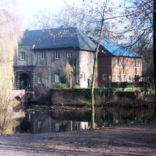 Historic building reflected in still water, surrounded by foliage.