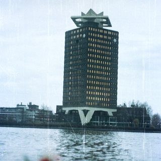 Tall building reflected in water with surrounding cityscape.
