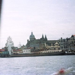 A boat travels along a canal with buildings in the background.