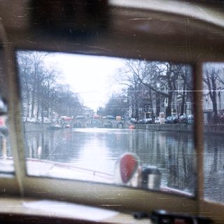 Canal scene with boats and buildings, viewed from a vehicle.