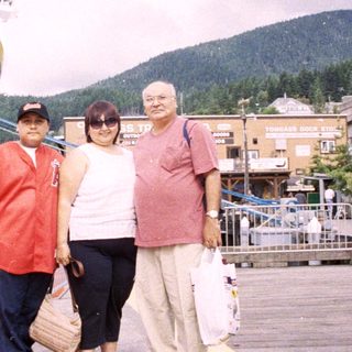 Here's a brief summary: Three people stand near a ship in a coastal town.