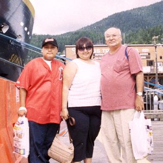 Here's a brief summary: Three people stand near a ship in a coastal town.