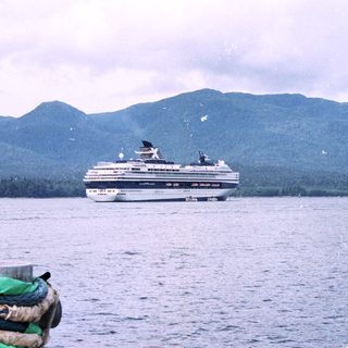 Cruise ship travels on water, with mountains in the background.