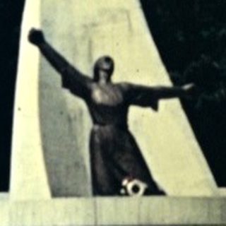 Monument with a figure stands on a path through trees.
