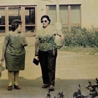 Two women stand near a fountain in front of a building.
