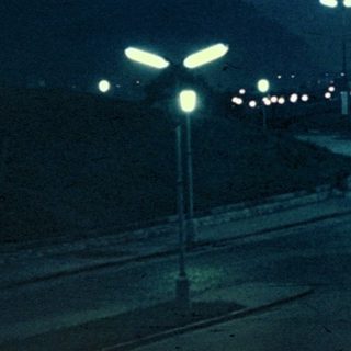 Night scene with streetlights, buildings, and distant hills.