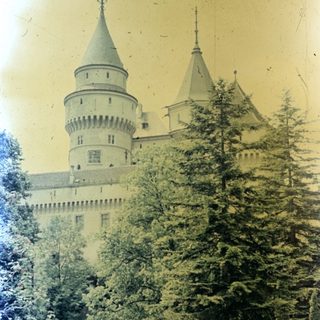 Castle with towers, seen through trees and foliage.
