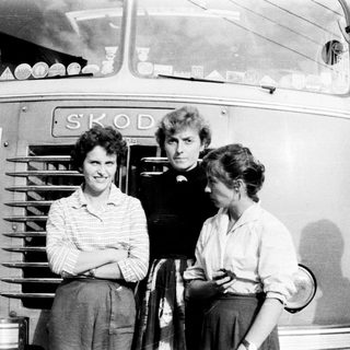 Three people stand beside a vintage Škoda bus.