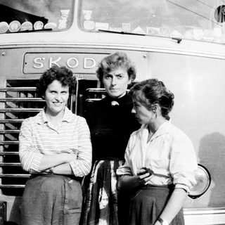 Three people stand beside a vintage Škoda bus.