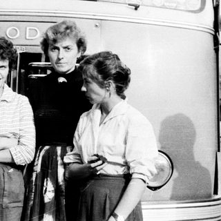 Three people stand beside a vintage Škoda bus.