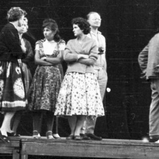 Group of people on a stage, in front of a dark backdrop.