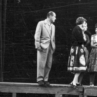 Group of people on a stage, in front of a dark backdrop.