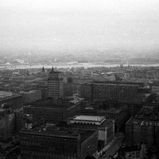 Here's a brief summary of the image: A cityscape with buildings, likely near a river, in monochrome.
