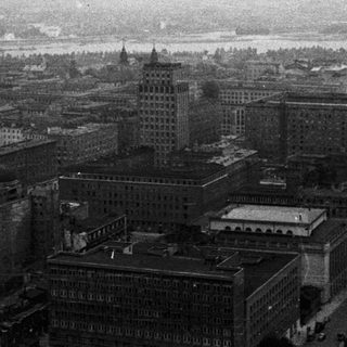 Here's a brief summary of the image: A cityscape with buildings, likely near a river, in monochrome.