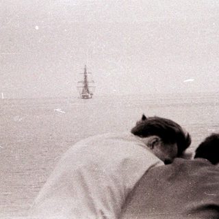People observe a ship at sea in a monochrome photo.