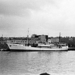 Ship docked at a pier with a building in background.