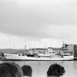 Ship docked at harbor, viewed from across the water.