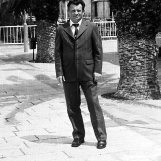 Man in suit stands near palm trees in a public space.