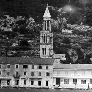 Building with tower near water, backed by hillside.