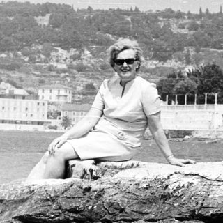 Woman sits on rocks overlooking a coastal town.