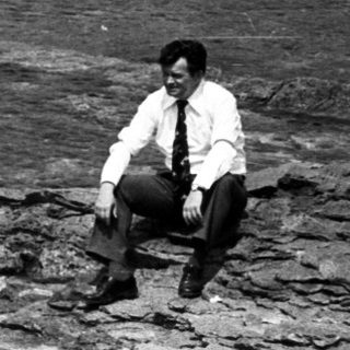 Man sits on rocks near the water's edge.