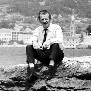 Man sits on rocks with a seaside town background.