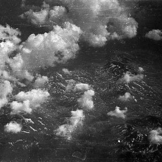 Aerial view of mountainous terrain with scattered clouds.