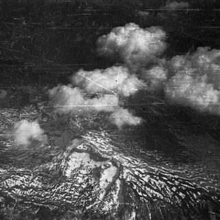 Here's a brief summary of the image: Snow-covered mountains and cloudscape in a black and white photograph.