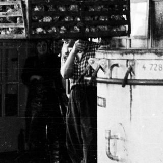 Black and white image of a wire cage suspended from a crane.