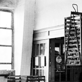 Black and white image of a wire cage suspended from a crane.