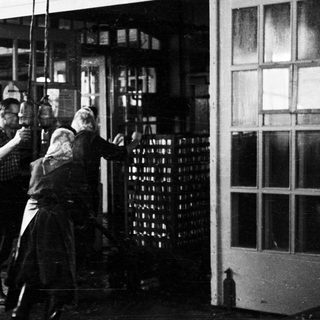 Men appear to be moving stacked bottles through a doorway.