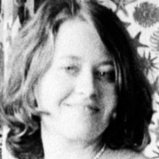 Woman seated in chair, posing near a patterned curtain.