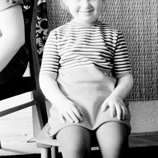 Here's a brief summary of the image: Young child sits on a chair, smiling for a portrait.