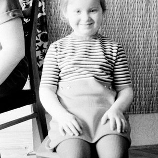 Here's a brief summary of the image: Young child sits on a chair, smiling for a portrait.