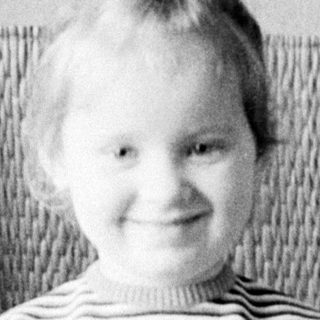 Here's a brief summary of the image: Young child sits on a chair, smiling for a portrait.