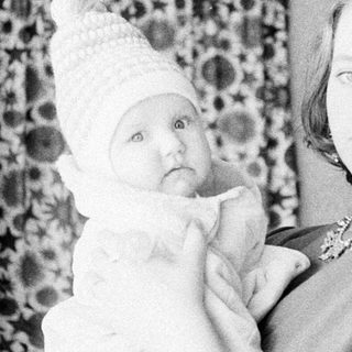 Woman holding baby, wearing a decorative hat.