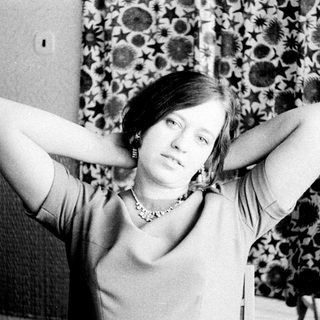 Woman with hands behind head, seated in a patterned chair.