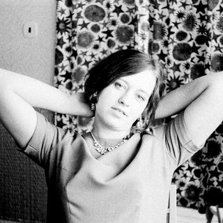 Woman with hands behind head, seated in a patterned chair.