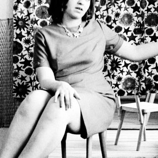 Woman in dress sits, posed in a vintage room.