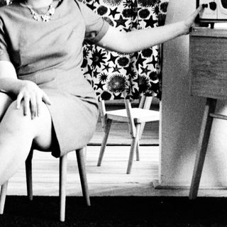 Woman in dress sits, posed in a vintage room.