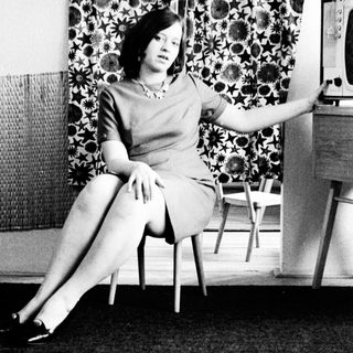 Woman in dress sits, posed in a vintage room.