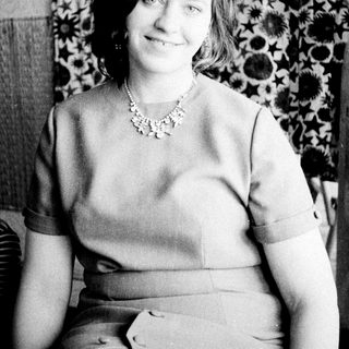 Woman in a necklace sits before a patterned wall.